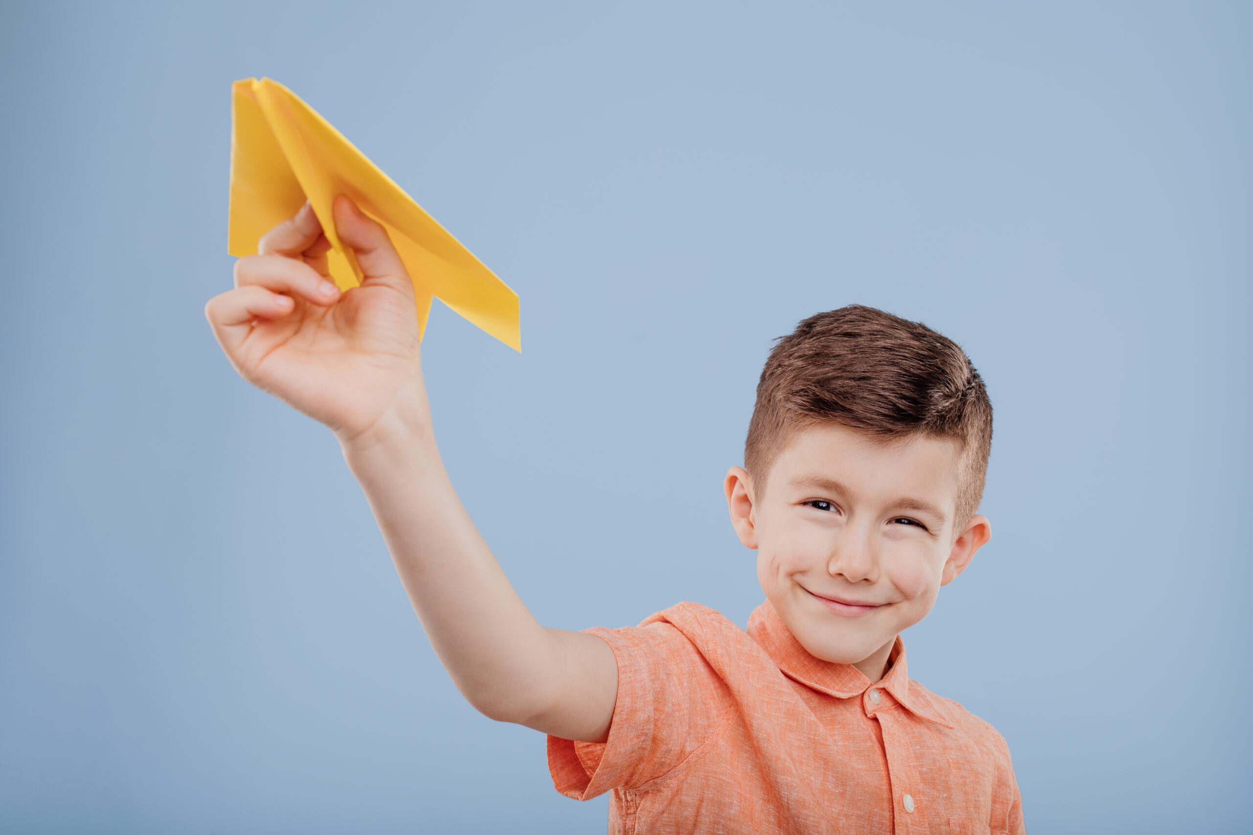 Junge spielt mit gelbem Papierflieger nach dem Origami Onlinekurs für Kinder