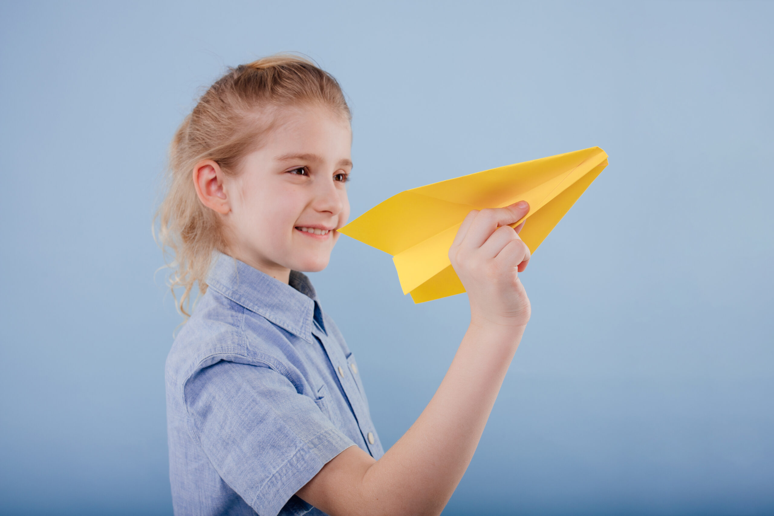 glückliches Kind Mädchen hält gelbes Papierflugzeug in der Hand, nachdem sie das Flugzeug gebastelt hat.